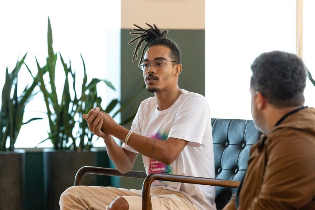 Um homem negro está sentado conversando com outras pessoas sobre um determinado tema.