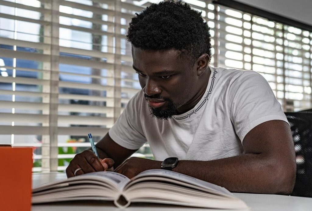 Um jovem homem negro está sentado estudando com a ajuda de um livro.